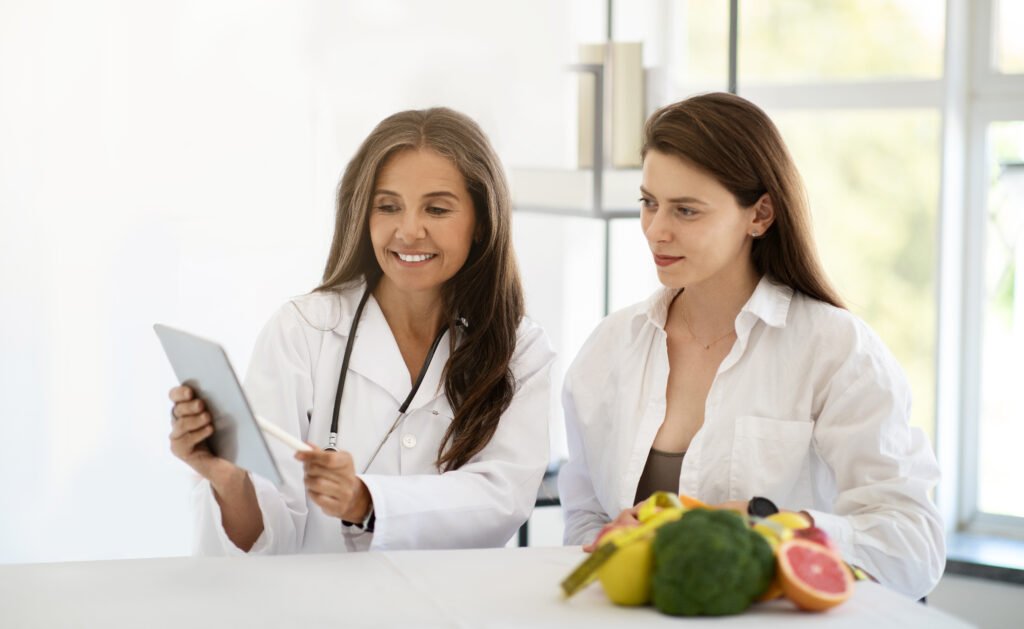 Cheerful adult caucasian doctor in white coat show tablet with weight loss plan to young patient in clinic office interior. Consultation, health care proper nutrition recommendation by professional