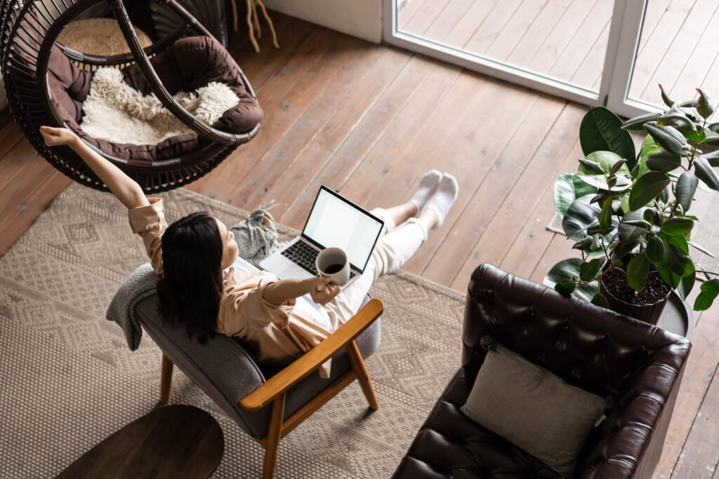 Happy free asian girl sitting at home with laptop and coffee mug, raising hands up.