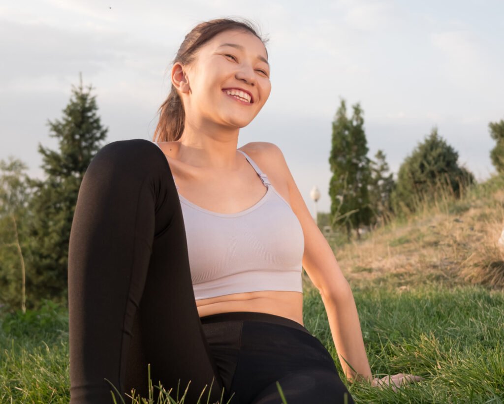 Asian girl in sportswear sits with a smile on the grass.