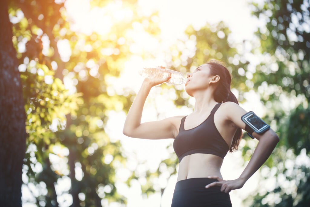 Fitness woman athlete takes a break, Drinking water, Hot day. Country rural road nature background.